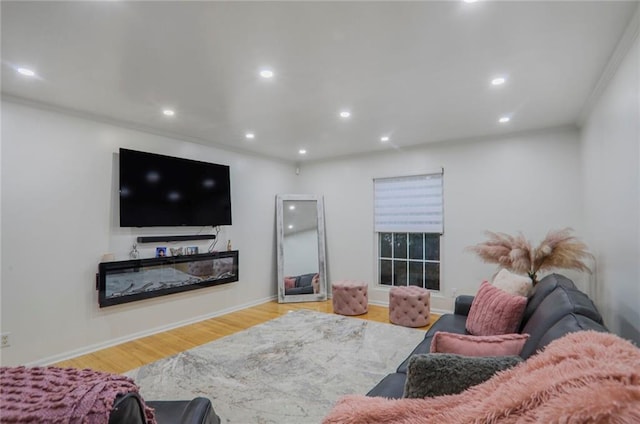 living room featuring baseboards, a glass covered fireplace, wood finished floors, crown molding, and recessed lighting