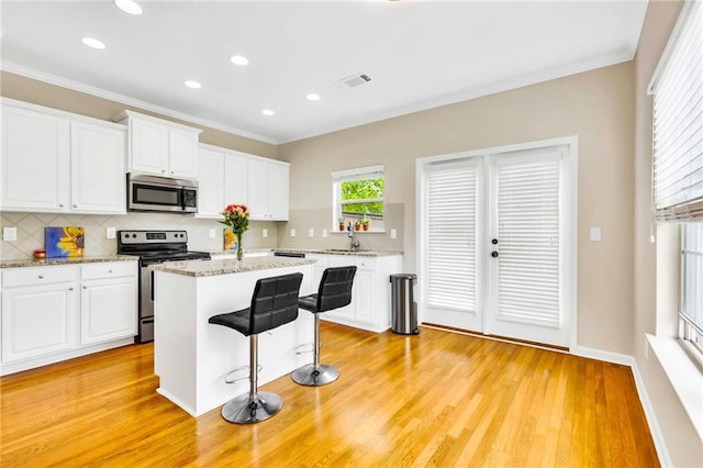 kitchen featuring white cabinetry, a center island, stainless steel appliances, and light stone counters