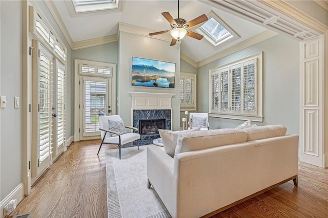 living room with light hardwood / wood-style flooring, crown molding, lofted ceiling with skylight, a fireplace, and ceiling fan