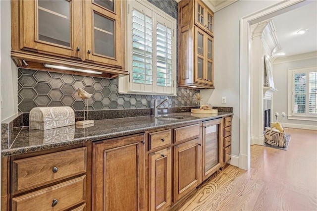 kitchen with wine cooler, dark stone counters, light hardwood / wood-style flooring, ornamental molding, and sink