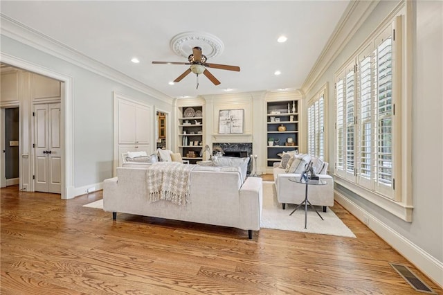 living room with light hardwood / wood-style floors, crown molding, built in shelves, and ceiling fan