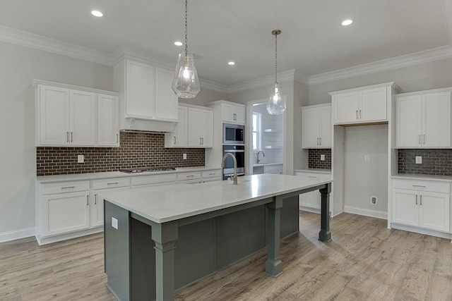 kitchen with white cabinetry, hanging light fixtures, stainless steel appliances, a center island with sink, and light wood-type flooring