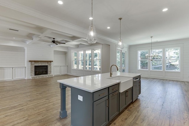 kitchen with sink, dishwasher, coffered ceiling, an island with sink, and decorative light fixtures