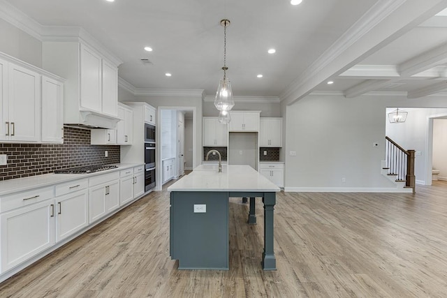 kitchen featuring stainless steel appliances, white cabinetry, a kitchen island with sink, and decorative light fixtures