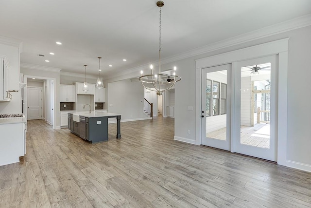 kitchen featuring hanging light fixtures, white cabinetry, a kitchen island with sink, and light hardwood / wood-style flooring