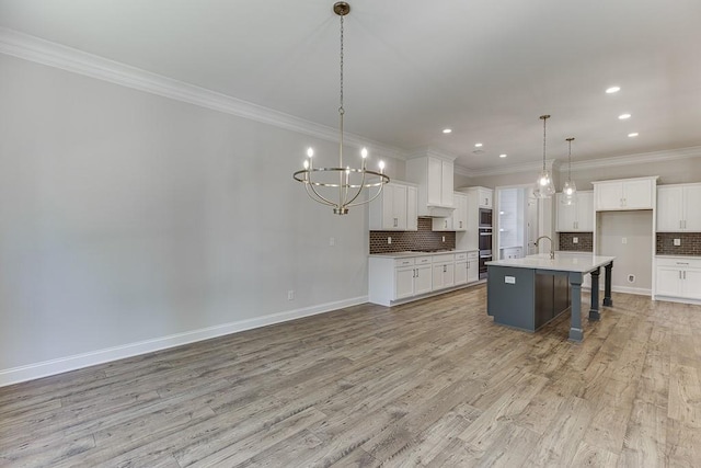 kitchen with pendant lighting, white cabinetry, a notable chandelier, an island with sink, and light wood-type flooring