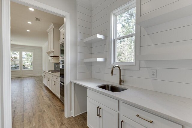 kitchen with light hardwood / wood-style floors, light stone countertops, sink, and white cabinets