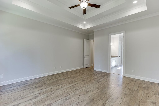 empty room with crown molding, ceiling fan, a tray ceiling, and light wood-type flooring