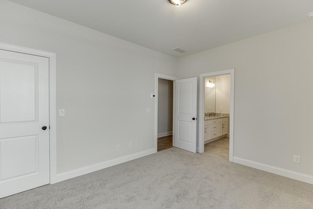 unfurnished bedroom featuring ensuite bath and light colored carpet