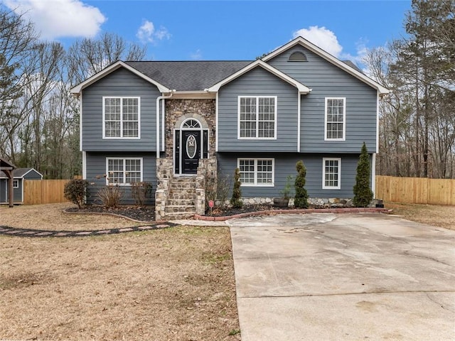 split foyer home with fence, stone siding, and roof with shingles