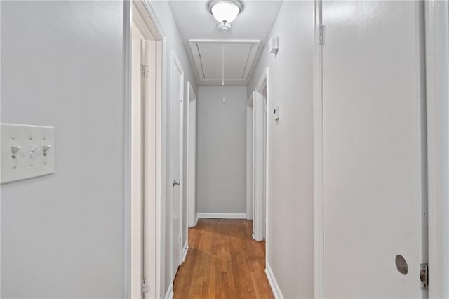 corridor with light wood-type flooring, attic access, and baseboards