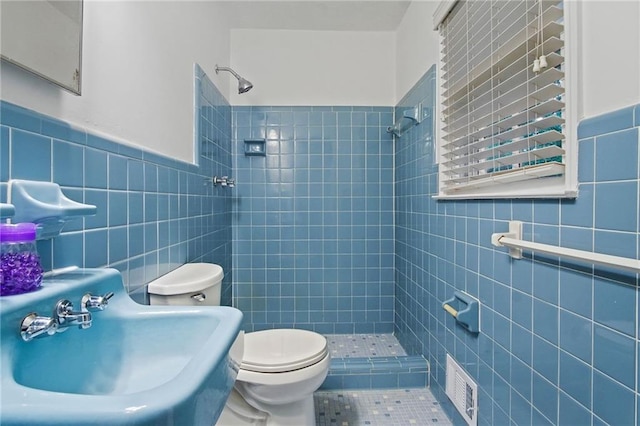 full bath with visible vents, toilet, a sink, a shower stall, and tile walls