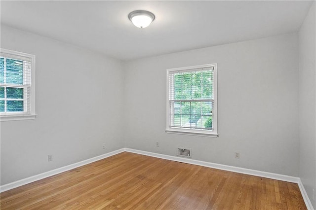 spare room with light wood-type flooring, visible vents, and baseboards