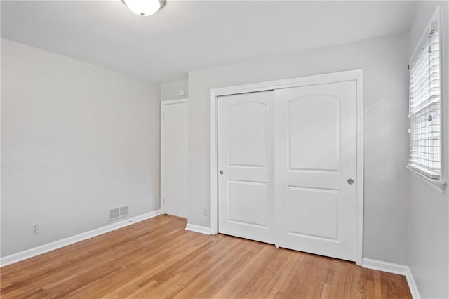 unfurnished bedroom with light wood-type flooring, a closet, visible vents, and baseboards