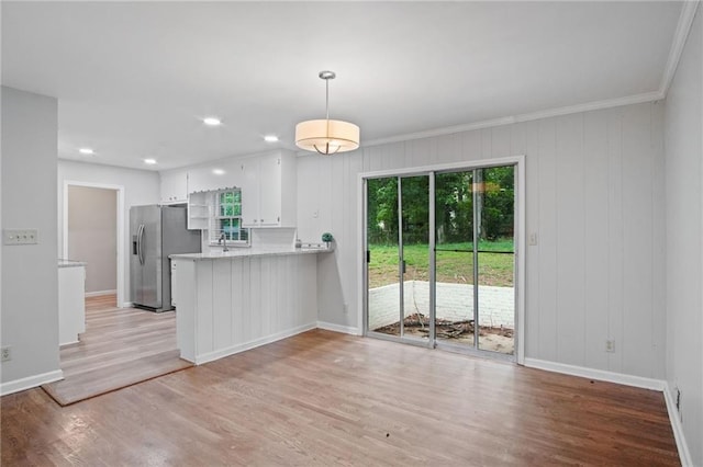 kitchen featuring a peninsula, white cabinetry, light wood-type flooring, stainless steel refrigerator with ice dispenser, and decorative light fixtures