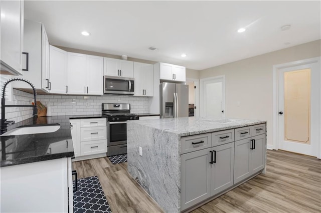 kitchen with sink, a kitchen island, stainless steel appliances, light stone countertops, and white cabinets