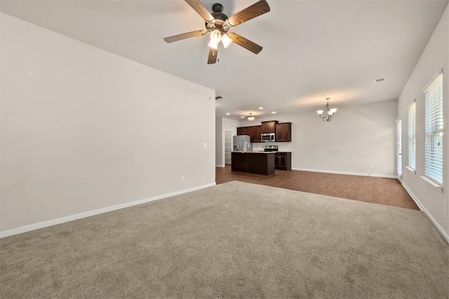 unfurnished living room with ceiling fan with notable chandelier and carpet flooring