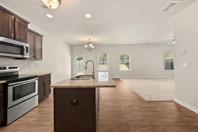 kitchen with stainless steel appliances, decorative light fixtures, light hardwood / wood-style flooring, dark brown cabinets, and a center island with sink