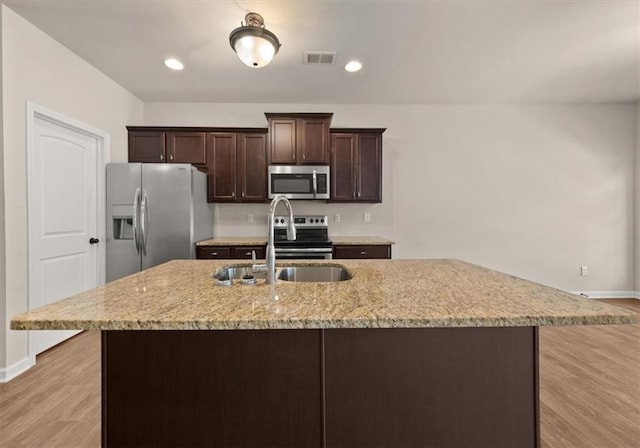 kitchen featuring stainless steel appliances, a center island with sink, light wood-type flooring, dark brown cabinetry, and sink