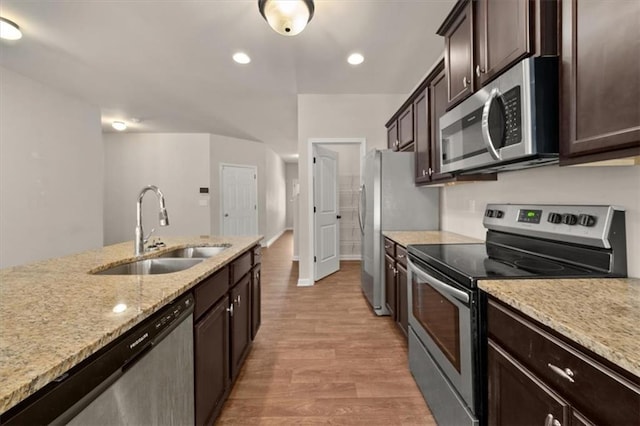 kitchen featuring appliances with stainless steel finishes, light hardwood / wood-style floors, light stone counters, sink, and dark brown cabinets