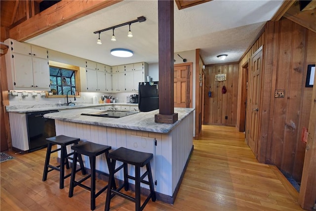 kitchen with light hardwood / wood-style flooring, wooden walls, light stone countertops, and black appliances