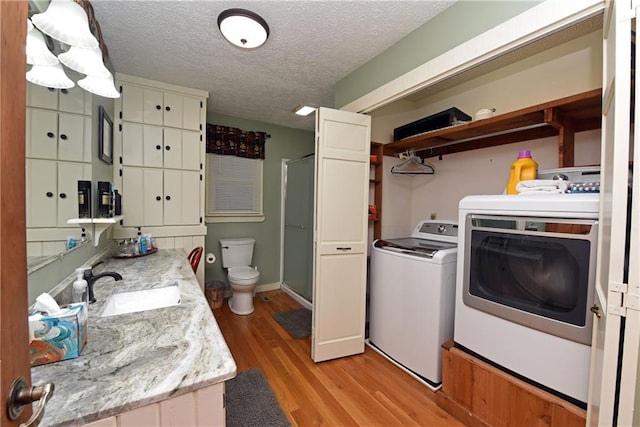 washroom with a textured ceiling, washer and clothes dryer, sink, and light hardwood / wood-style flooring