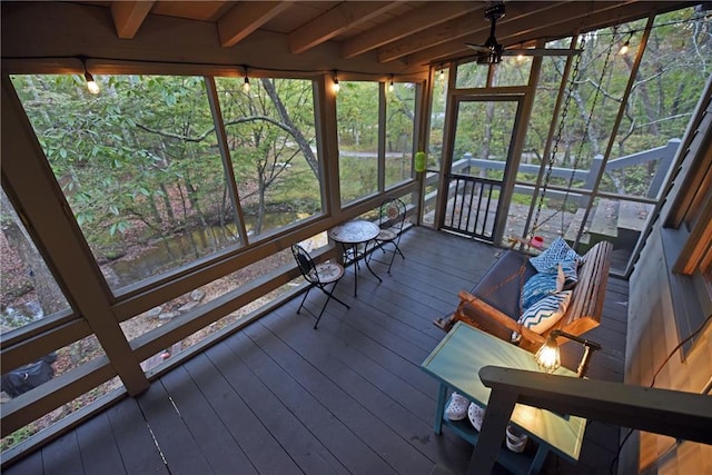 unfurnished sunroom with ceiling fan, beamed ceiling, and a wealth of natural light