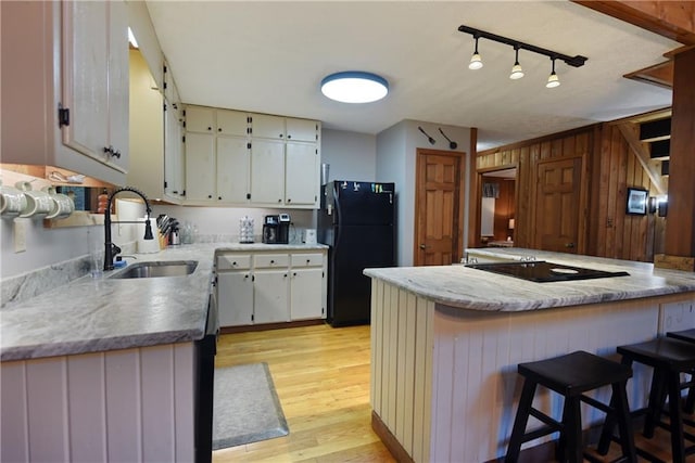 kitchen featuring light hardwood / wood-style floors, sink, kitchen peninsula, black refrigerator, and a kitchen bar