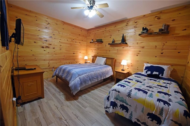 bedroom with ceiling fan, light hardwood / wood-style flooring, and wood walls