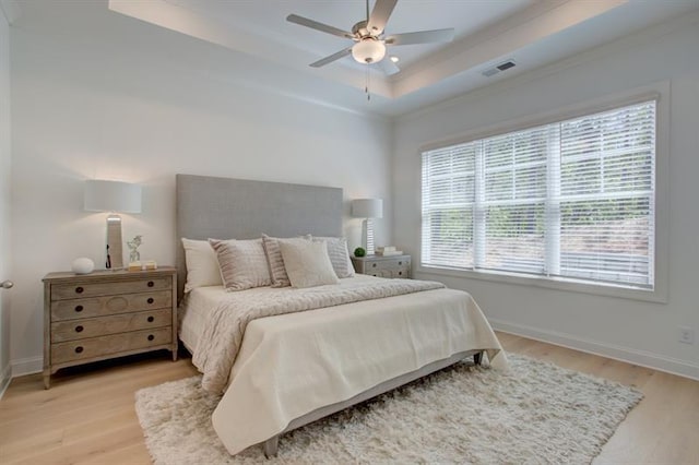 bedroom featuring a ceiling fan, baseboards, visible vents, a tray ceiling, and light wood-style flooring