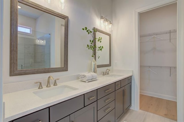 bathroom with double vanity, a spacious closet, a stall shower, and a sink