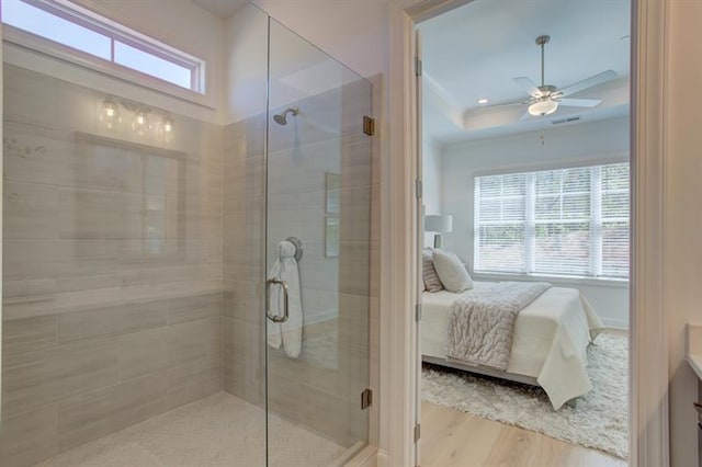 bathroom with a shower stall, connected bathroom, wood finished floors, a raised ceiling, and a ceiling fan