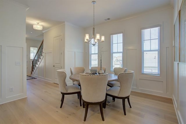 dining space with light wood-style floors, crown molding, stairs, and a decorative wall