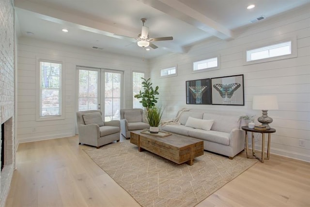 living room with beamed ceiling, visible vents, a fireplace, light wood finished floors, and baseboards