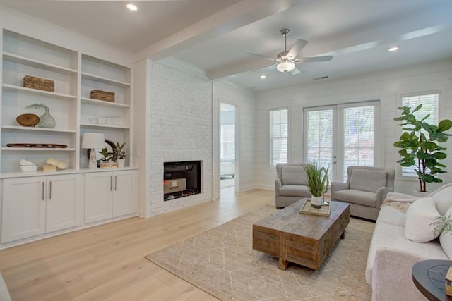 living room with ceiling fan, beamed ceiling, a stone fireplace, recessed lighting, and light wood-style flooring