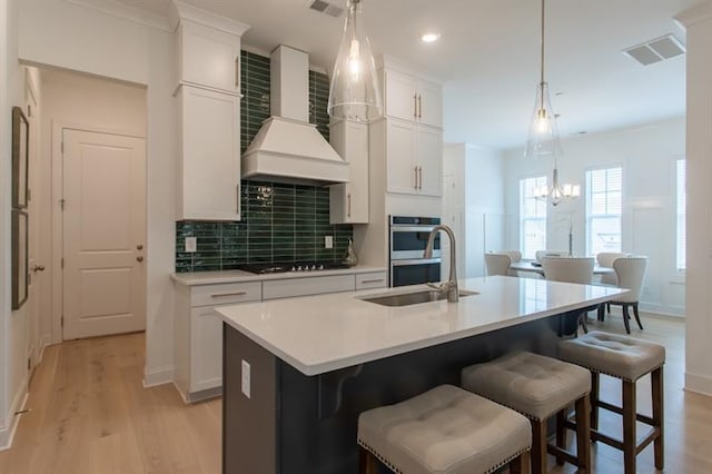 kitchen with a sink, black stovetop, light countertops, wall chimney exhaust hood, and a kitchen island with sink