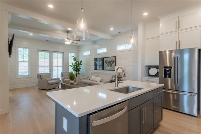 kitchen with beam ceiling, a sink, stainless steel appliances, light wood finished floors, and light countertops