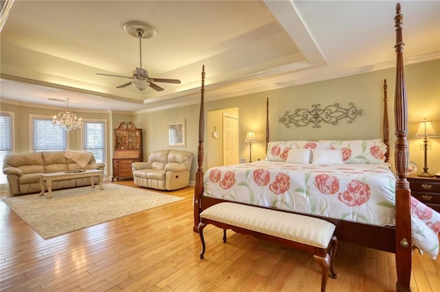 bedroom featuring ceiling fan with notable chandelier, ornamental molding, light hardwood / wood-style flooring, and a tray ceiling