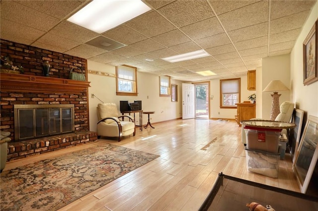 living room with a drop ceiling, light hardwood / wood-style flooring, and a brick fireplace