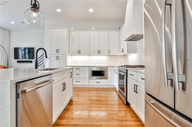 kitchen featuring sink, decorative light fixtures, light wood-type flooring, stainless steel appliances, and white cabinets