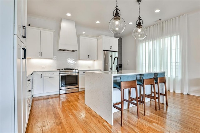 kitchen with premium range hood, stainless steel appliances, an island with sink, and white cabinets