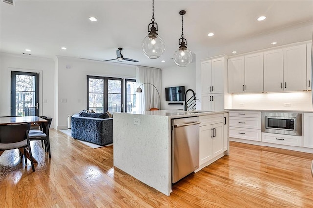 kitchen featuring sink, white cabinetry, decorative light fixtures, appliances with stainless steel finishes, and a kitchen island with sink