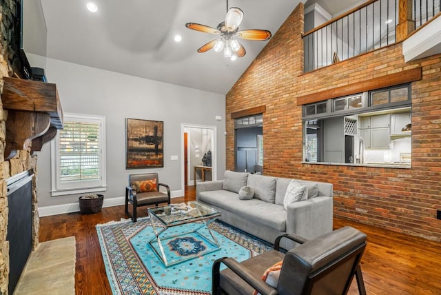 living room with a fireplace, ceiling fan, dark hardwood / wood-style floors, high vaulted ceiling, and brick wall