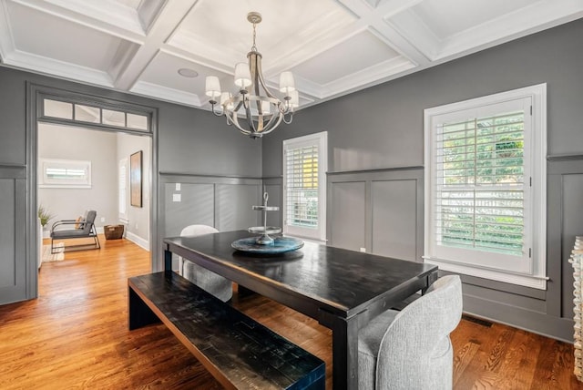 dining room featuring hardwood / wood-style floors, coffered ceiling, beamed ceiling, a notable chandelier, and ornamental molding