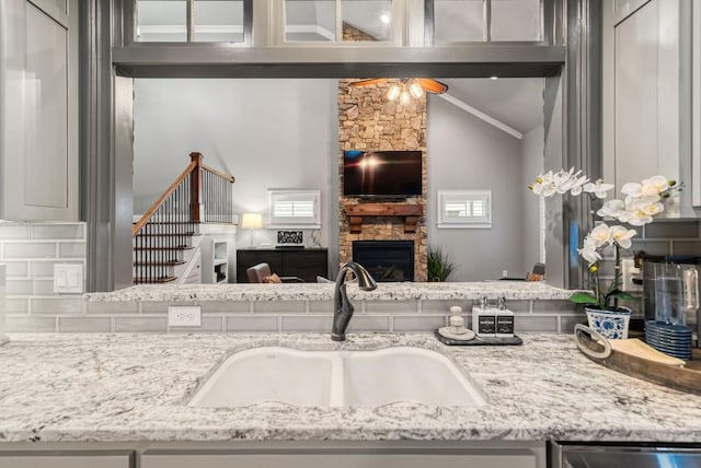 kitchen with light stone countertops, sink, a fireplace, and vaulted ceiling