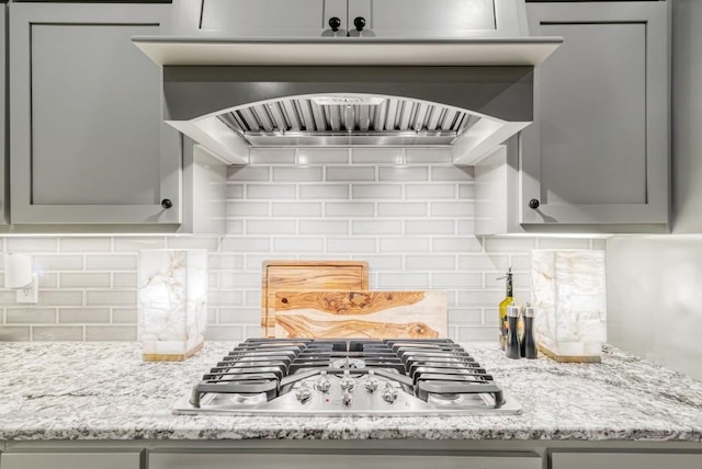 kitchen featuring backsplash, light stone countertops, gray cabinets, and stainless steel gas stovetop