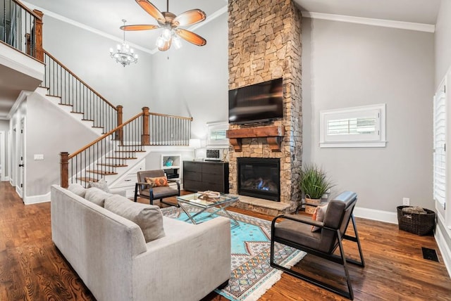 living room with dark wood-type flooring, a stone fireplace, a towering ceiling, and ornamental molding