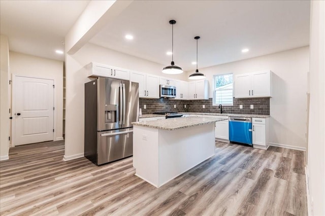 kitchen with appliances with stainless steel finishes, white cabinetry, hanging light fixtures, a kitchen island, and decorative backsplash