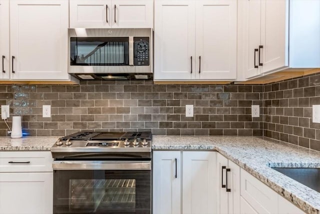 kitchen with appliances with stainless steel finishes, white cabinets, light stone counters, and decorative backsplash