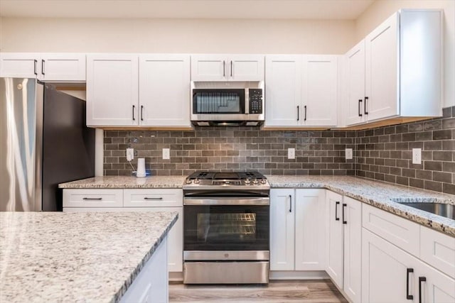 kitchen with backsplash, stainless steel appliances, light stone counters, white cabinets, and light wood-type flooring